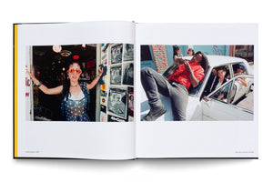 An open photobook displays two color photographs on facing pages. On the left, a woman in large, round orange sunglasses stands in a doorway covered in posters. On the right, a group of young people hang out on and in a white car on a city street.