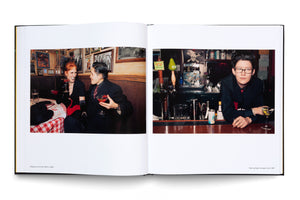 An open book displays two color photographs from the late 1990s. On the left, a smiling woman with red hair and a person in a dark suit share cocktails in a restaurant booth. On the right, a person with glasses and dark hair leans on a bar, looking at the camera with a martini in front of them.