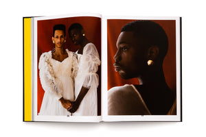 An open art book on a white surface, displaying a two-page spread. On the left, two androgynous people of color in white, ruffled dresses hold hands against a red background. The right page shows a close-up profile portrait of one of the individuals, highlighting their face and a gold earring.
