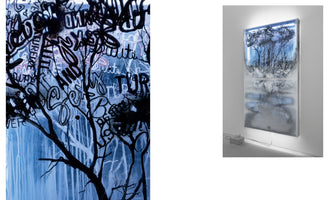 A side-by-side view of two contemporary artworks featuring silhouetted trees. The image on the left is a close-up of a painting with black tree branches overlaid with dense, layered graffiti tags against a streaky blue and white background. On the right is a full view of a tall, vertical light box mounted on a wall, illuminating a serene and misty landscape of trees reflected in water.