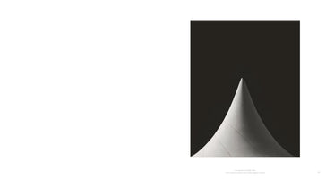 A minimalist black and white photograph showing a white, cone-shaped sculpture with a sharp tip and a wide, curving base. The object is set against a solid dark background, with dramatic side lighting that highlights its textured surface and elegant form. The photo is on the right page of an open book.