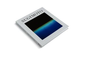 An angled, overhead shot of a square hardcover book titled SUGIMOTO on a plain white background. The book has a light grey cover featuring a square abstract photograph with a color gradient from black to deep blue. The spine reads HIROSHI SUGIMOTO TIME MACHINE.