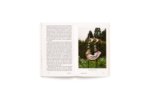 An open book showing pages 98 and 99. The left page has a column of text about motherhood. The right page displays a color photograph of a tall, abstract bronze sculpture standing in a garden with green bushes and white flowers. The caption reads, Mon corps de femme, 2019, and Mother of Tears.