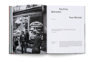 An open book showing a two-page spread. The left page has a full-bleed, black-and-white photograph of men in early 20th-century attire standing on a cobblestone street in front of a shop with Hebrew writing on the window. The right page has the title Soutine, Between Two Worlds by Pascale Samuel, followed by introductory text.