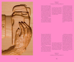A two-page spread from a book. The left page shows an intricate wood carving of a hand holding a DSLR camera against a pink background. The right page is filled with columns of text in both Danish and English.