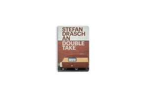 The book cover for Stefan Drasch An Double Take, set against a plain white background. The cover features a photograph of a vintage brown and beige camper trailer parked in front of a red brick wall, with the title and author's name in a large, brown, sans-serif font at the top.