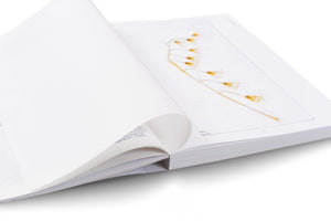A high-angle, close-up shot of an open book with white pages on a white background. The page on the right displays a delicate botanical image of a single, arching stem with several translucent, yellow, bell-shaped flowers. A blank page on the left is slightly curled as if being turned.
