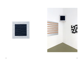 A two-page spread from a book. The left page shows a close-up of a square, textured artwork with a dark navy center and a white border. The right page shows an installation view of a white gallery corner displaying three abstract artworks: the same square piece from the left, a large rectangular piece with horizontal wood and silver stripes, and a piece with a jagged black and white pattern.