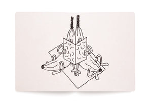 A whimsical black ink drawing in an open sketchbook shows two surreal, dog-like creatures joined at the head. They sit back-to-back, sharing and reading a single open book, while their long bodies splay out symmetrically on a square surface.