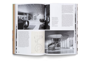 An open architecture book with a green spine lies on a white background. The pages feature a layout with German text, black-and-white photographs, and technical drawings of a mid-century modern interior. The images show a spacious lobby with distinctive lounge chairs and a prominent, elegant spiral staircase.