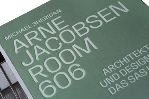 A close-up, angled photograph of a book cover with a textured, sage green surface. The title, ARNE JACOBSEN ROOM 606 by MICHAEL SHERIDAN, is printed in a raised, white, sans-serif font. A portion of a subtitle in German is also visible.