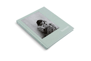 A hardcover book with a pale green cloth cover, titled human, rests on a white background. The cover features an inset black-and-white photograph of two young people in patterned clothes sitting closely together against a textured wall.