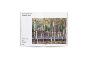 An open book on a white background. The left page has German text with the heading KUNSTPAUSE atelier le balto. The right page shows a photograph of a wooden boardwalk running through a dense forest of thin birch trees in autumn.