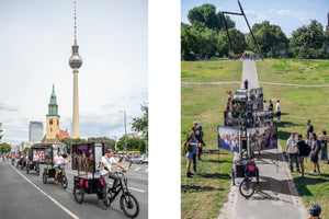 A diptych showing a mobile photography exhibition in Berlin. On the left, a parade of cargo tricycles with large photo displays rides on a street with the Berlin TV Tower in the background. On the right, the same tricycles are parked on a path in a grassy park, forming an outdoor gallery that people are gathered around to view.