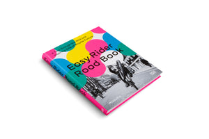An angled, overhead view of the hardcover book Easy Rider Road Book against a white background. The cover features a bold design with large, overlapping circles in pink, yellow, blue, and teal. A dynamic black-and-white photograph of a cyclist doing a wheelie on a city street is overlaid with the title. The book has a bright pink spine and edges.