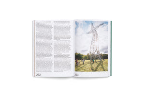 An angled view of an open book showing pages 262 and 263. The left page is filled with text, while the right page displays a large photograph of a towering, twisted metal lattice sculpture in a grassy field. A small group of people with bicycles are gathered at the base of the sculpture.
