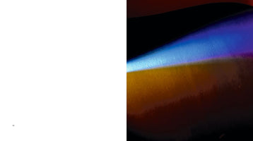 A two-page book spread. The left page is entirely white, with the page number 188 at the bottom-left corner. The right page is a full-bleed, close-up, abstract photograph of a dark, glossy surface with a diagonal band of iridescent light that shifts in color from bright blue and purple to a warm golden-orange against a black background.