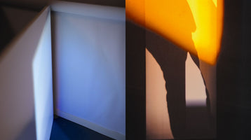 A side-by-side image showing two abstract views of an architectural corner with different lighting. On the left, the corner is lit with a soft, cool blue light. On the right, the corner is lit by a warm, intense orange-yellow light that casts strong, dark shadows.