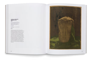A photograph of an open art book. The page on the right displays a dark, textured print of a seated nude woman from behind, her back illuminated with a golden light. Beside her is a piece of green fabric. The left page contains descriptive German text about the artwork.