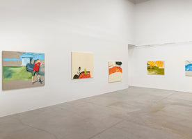 An interior shot of a spacious modern art gallery with white walls and a concrete floor. Several contemporary paintings of varying sizes are hung on the walls, featuring a mix of figurative and abstract styles with bold colors.