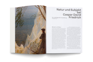 An open art book or exhibition catalog, viewed from an angle. The left page features a painting by Caspar David Friedrich of a man in a dark coat and cap, seen from behind, standing on a white chalk cliff and looking out over the sea. The right page has German text under the title Natur und Subjekt bei Caspar David Friedrich.