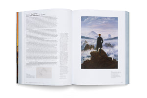 An open art book displaying a two-page spread on a white surface. The right page features Caspar David Friedrich's painting, Wanderer above the Sea of Fog, showing a man from behind standing on a rocky precipice overlooking a misty mountain landscape. The left page contains German text and a small sketch.