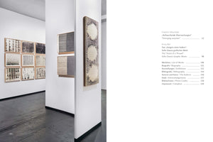 A two-page spread from an art book. The left page is a photograph of an art gallery with white walls and a dark floor. Abstract, mostly black-and-white artworks hang on the walls, including a grid of twelve smaller framed pieces and several larger, textured works. The right page shows the book's table of contents in German and English, listing chapters and sections like Biography, List of Works, and Exhibitions with their corresponding page numbers.