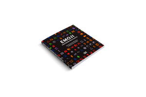 A paperback book titled EMOJI VON SHIGETAKA KURITA lies at an angle on a white background. Its black cover is decorated with a colorful grid of the original pixelated emoji icons.