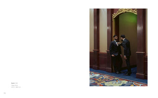 A book spread with text on the left and a photograph on the right. The photo shows two men in black tuxedos standing in an ornate, wood-paneled hallway. One man helps the other adjust his bow tie inside a doorway with a decorative gold arch. A green light illuminates the space behind them, and a colorful floral carpet covers the floor.