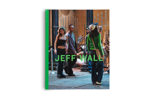 The book Jeff Wall, with a bright green spine, displayed on a white background. The cover features a photograph of a group of people on a city sidewalk at night in front of a metal fence. A woman seen from the back wears a green shirt and a trucker hat, and the title JEFF WALL is written across the image in large green letters.