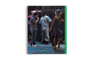 A grainy, full-color photograph on a book cover with a green spine. The photo shows a candid street scene at night. A woman with short, blue-tipped hair and shiny gold heels walks to the right, passing a diverse group of people socializing on a sidewalk littered with cigarette butts.