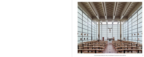 The interior of a modern church with rows of simple wooden pews facing the altar. The room is filled with light from tall, translucent walls made of gridded panels. A large crucifix hangs from the exposed concrete ceiling in the center of the symmetrical space.