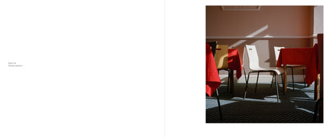 An open book with a photograph on the right-hand page. The photo shows an empty dining area where a sharp, diagonal beam of sunlight streams in, illuminating a white chair and a table with a bright red tablecloth. The furniture casts long, dark shadows across the patterned carpet.