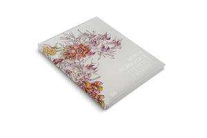 A light gray hardcover book, Miron Schmückle Flesh for Fantasy, is displayed at an angle on a white surface. The cover features an intricate, colorful illustration of surreal, fantastical flowers in shades of red, yellow, and purple, arranged along the left side, with the title in a simple font on the right.