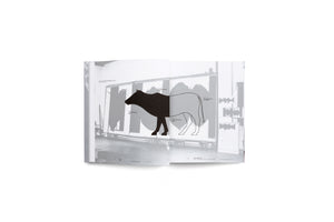 An open art book is displayed against a white background. The two-page spread shows a black and white graphic of a cow. The front half of the cow is a solid black silhouette, while the back half is a simple outline. This image is superimposed on a photograph of an artist's studio with large canvases. German text labels point to different parts of the cow.