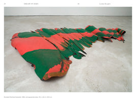 A gallery photograph of Lynda Benglis's 1968 sculpture, Rumpled Painting/Caterpillar. A long, low-lying artwork made of cast pigmented latex rests on a concrete floor. Its undulating, segmented form is painted in bold, organic patches of bright red-orange and dark green.