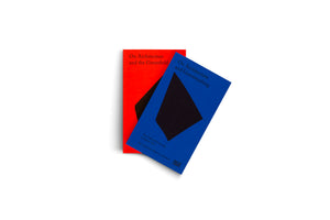 Two paperback books with minimalist covers are displayed against a plain white background. A bright red book, titled On Architecture and the Greenfield, is mostly covered by a vibrant blue book placed on top at an angle. The blue book's cover reads On Architecture and Greenwashing and features a large black diamond shape.