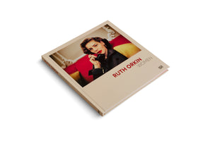 A square hardcover book with a beige cover, titled RUTH ORKIN WOMEN, resting on a white surface. The cover features a color photograph of a woman with styled dark hair and red lipstick, holding a vintage black telephone to her ear while sitting on a red and yellow couch.