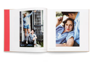 An open photobook on a white surface displays two vintage-style color photographs on facing pages. The photo on the left shows a woman in a hat pointing upwards while a man sits on a porch step below her, smoking. The photo on the right is an intimate close-up of a woman in a striped shirt being embraced by a man.