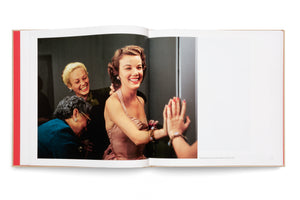 An open book lies flat, displaying a vintage color photograph of actress Nanette Fabray from 1952. She wears a pink satin dress and laughs joyfully while looking at her reflection. Two other women stand smiling behind her in a candid backstage moment.
