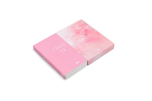 An isometric view of the pink art book ZHOU LI, partially slid out of its matching slipcase. The book cover is solid pink, while the slipcase has an abstract watercolor design in lighter pink and white. The book is set against a plain white background.