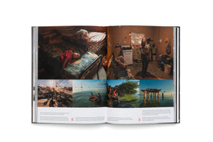 An open photobook displays a two-page spread with a collage of documentary-style photographs. The top half features two large images of people inside modest homes. The bottom half shows four smaller images of outdoor scenes, including people near a polluted body of water and at a street market. English captions are printed below the images.