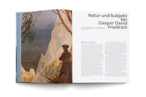 An angled photo of a two-page spread in an open art book. The left page features a painting by Caspar David Friedrich showing a man from behind looking out over white chalk cliffs to the sea. The right page contains German text with the title Natur und Subjekt bei Caspar David Friedrich.