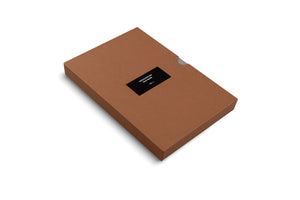 A flat, rectangular brown cardboard slipcase box is shown at an angle on a white background. A black label on the top reads in white text, Frequencies, Oscar Murillo, VOL. I.