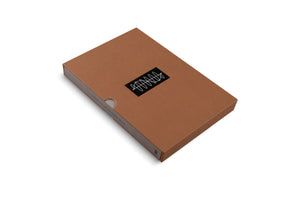A light brown, rectangular cardboard box with a lid, photographed from an angle against a plain white background. A black rectangular sticker is centered on the lid, featuring a white, abstract, continuous squiggly line.