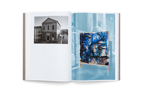 An open book on a white background. The left page features a black-and-white photograph of a historic brick building next to a canal. The right page shows a large abstract painting with bold blue and black strokes on a wooden stand, set against a blue-tinted image of an architectural interior with columns.