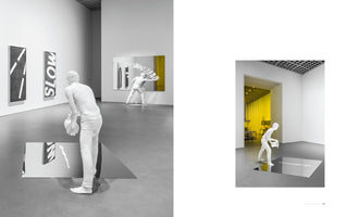 A black-and-white diptych showing a modern art exhibition in a gallery. On the left, two all-white, life-sized sculptures of men interact with mirrored surfaces on the wall and floor. On the right, one of the sculptures bends to pour a white liquid onto a mirror embedded in the floor, with a view into a bright yellow room in the background.