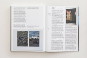 An open art book laid flat, showing a two-page spread. The left page, 214, has English text and two photos of a shoe in flowers and a street scene. The right page, 215, has German text and a larger photo of a Sparkasse bank storefront with graffiti on the window.