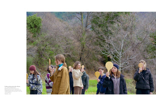 An outdoor photograph shows a group of young people standing in a grassy, wooded area. They are all holding small, paddle-shaped wooden hand mirrors up to their faces. To the left of the image is a block of text that titles the activity Walking Backwards with a Mirror and provides instructions.