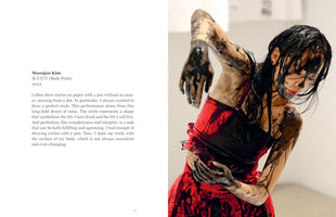 A two-page spread from a book. The left page contains text about Moonjoo Kim's artwork, Body Print. The right page is a photograph of Kim, an East Asian woman in a red dress, her face, arms, and hair streaked and dripping with thick black paint. She stands in a dynamic, expressive pose against a white background, her head bowed and arms bent as if in a performance.